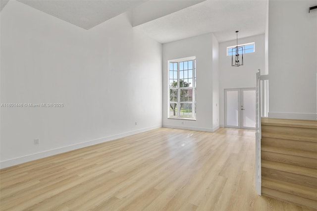 8501 NW 191st St, Hialeah, FL 33015 - unfurnished living room featuring light wood-style floors, french doors, baseboards, a high ceiling, and a chandelier