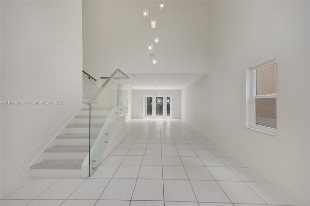 stairway with tile patterned floors, a chandelier, a towering ceiling, and baseboards