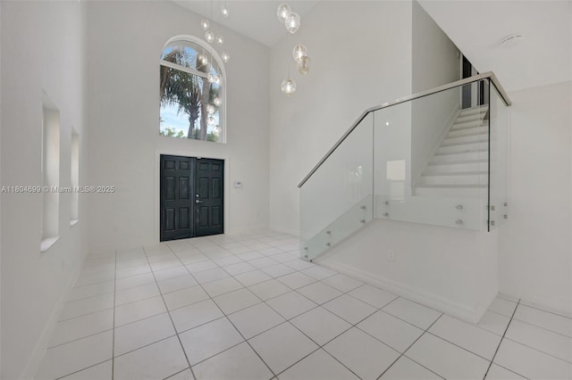 entryway featuring a towering ceiling, stairs, tile patterned floors, and baseboards