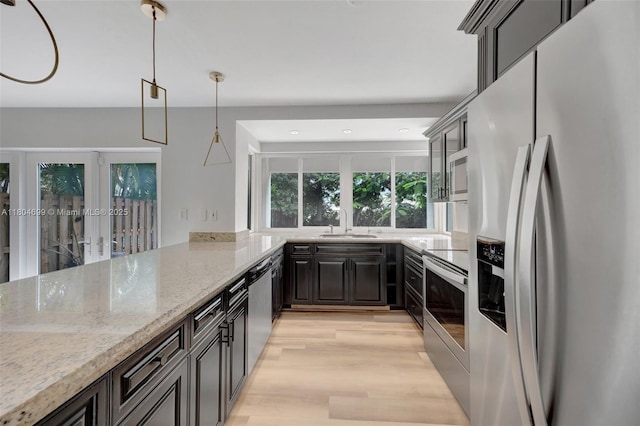 kitchen featuring stainless steel appliances, a sink, light wood finished floors, recessed lighting, and light stone countertops