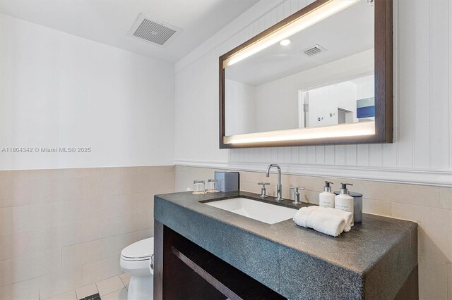 17315 Collins Ave Unit 1008, Sunny Isles Beach, FL 33160 - half bath featuring tile walls, toilet, vanity, tile patterned flooring, and a wainscoted wall