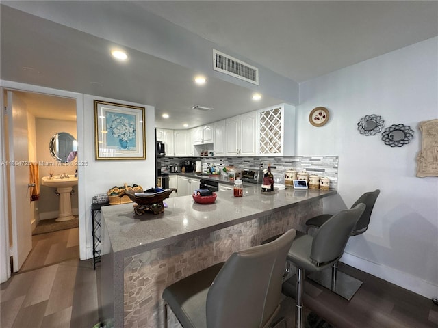 14367 SW 96th Ln, Miami, FL 33186 - kitchen with baseboards, a breakfast bar area, a peninsula, white cabinetry, and wood finished floors
