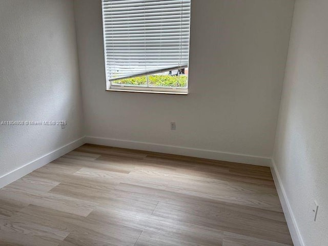spare room featuring baseboards and light wood finished floors