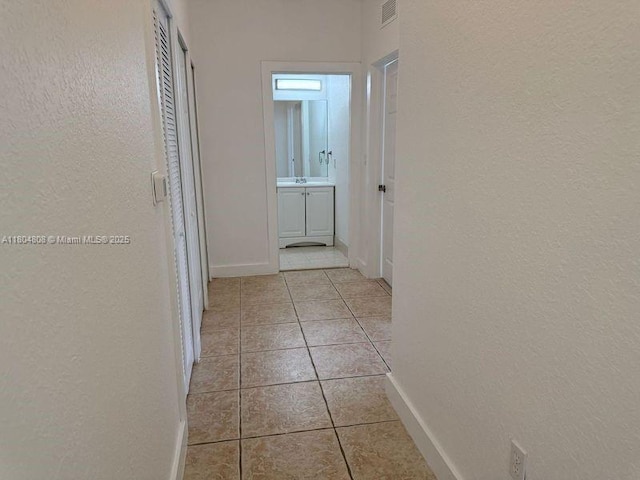 hall with a textured wall, baseboards, and light tile patterned floors