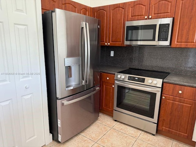 kitchen featuring stainless steel appliances, dark countertops, light tile patterned floors, and brown cabinets