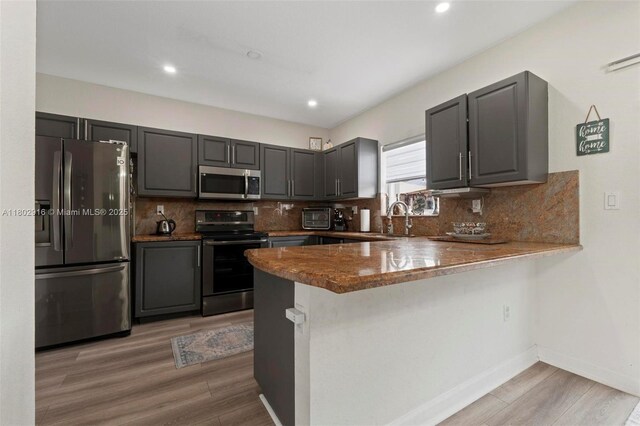 922 SW 148th Pl, Miami, FL 33194 - kitchen featuring appliances with stainless steel finishes, light wood-type flooring, a sink, a peninsula, and decorative backsplash