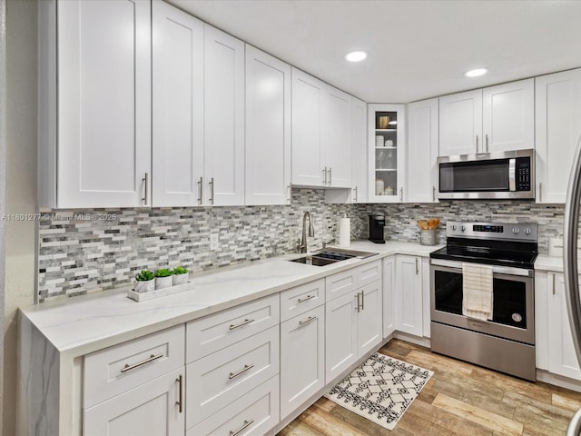 kitchen featuring stainless steel appliances, a sink, white cabinets, glass insert cabinets, and decorative backsplash