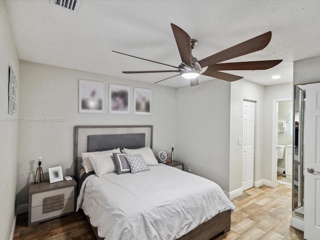 bedroom featuring wood finished floors, baseboards, ensuite bath, and ceiling fan