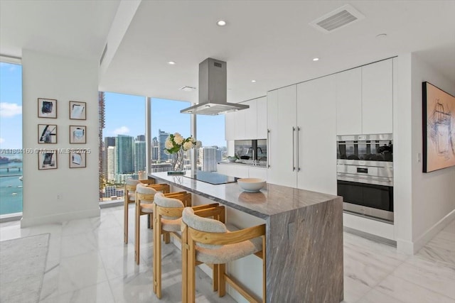 700 NE 26th Ter Unit 3903, Miami, FL 33137 - kitchen featuring island exhaust hood, a kitchen breakfast bar, a kitchen island, light marble finish flooring, and white cabinetry