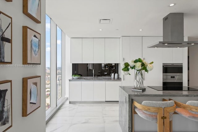700 NE 26th Ter Unit 3903, Miami, FL 33137 - kitchen with island range hood, light marble finish flooring, modern cabinets, black electric stovetop, and expansive windows