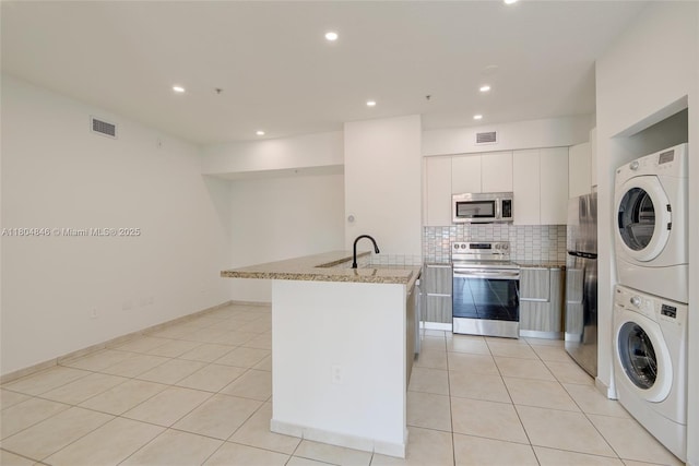 7330 NW 114th Ave Unit 304-5, Doral, FL 33178 - kitchen with stainless steel appliances, estacked washer and dryer, backsplash, light stone countertops, and white cabinetry
