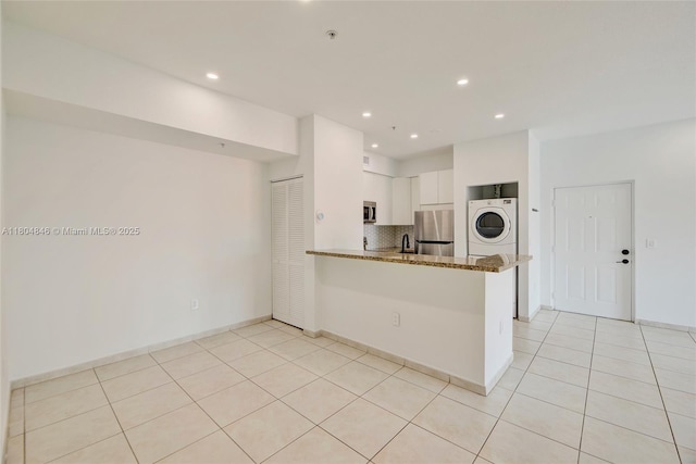 7330 NW 114th Ave Unit 304-5, Doral, FL 33178 - kitchen with stainless steel appliances, stacked washing machine and dryer, dark stone counters, white cabinets, and decorative backsplash