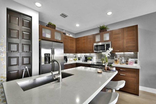 15678 NW 91st Ct, Miami Lakes, FL 33018 - kitchen featuring stainless steel appliances, a kitchen breakfast bar, tasteful backsplash, glass insert cabinets, and recessed lighting