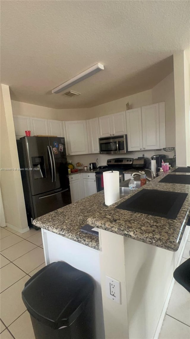 9942 SW 158th Ct, Miami, FL 33196 - kitchen featuring appliances with stainless steel finishes, light tile patterned floors, a peninsula, a textured ceiling, and white cabinets