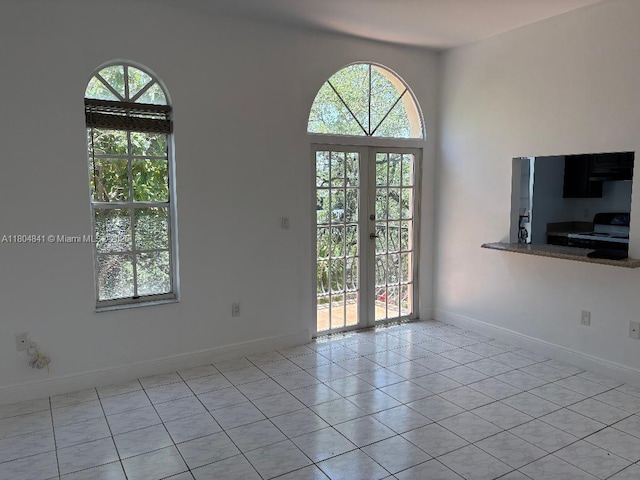 tiled empty room featuring plenty of natural light, french doors, and baseboards