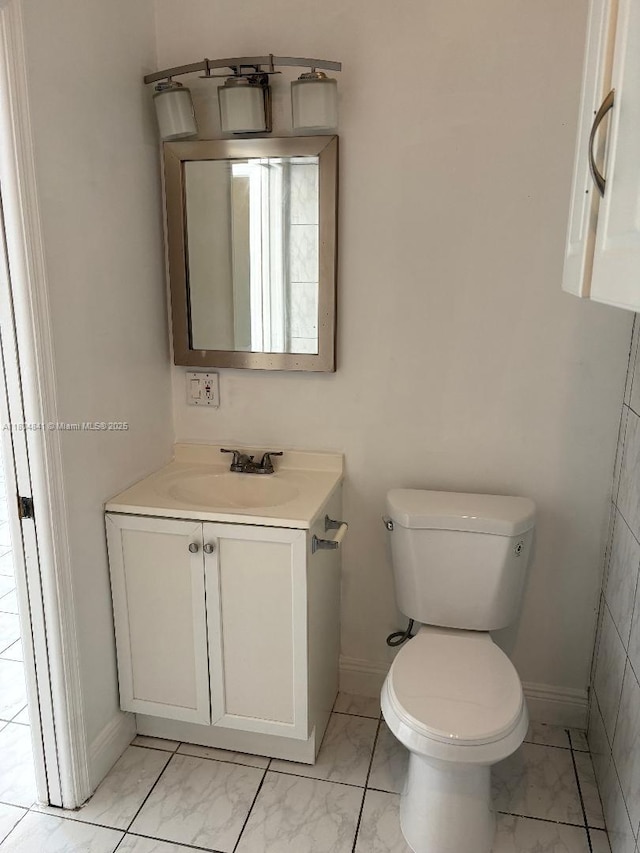 bathroom featuring marble look tile flooring, toilet, baseboards, and vanity