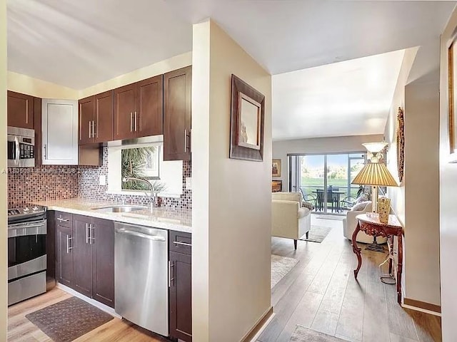 kitchen featuring appliances with stainless steel finishes, a sink, light wood-type flooring, open floor plan, and dark brown cabinets