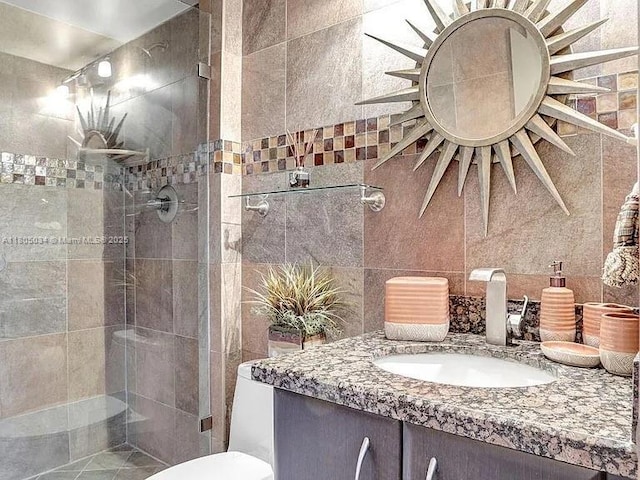 full bathroom featuring tiled shower, vanity, toilet, and tile walls