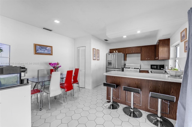 2023 SW 99th Ave, Miami, FL 33165 - kitchen featuring stainless steel fridge, white range with gas cooktop, light countertops, recessed lighting, and a kitchen bar
