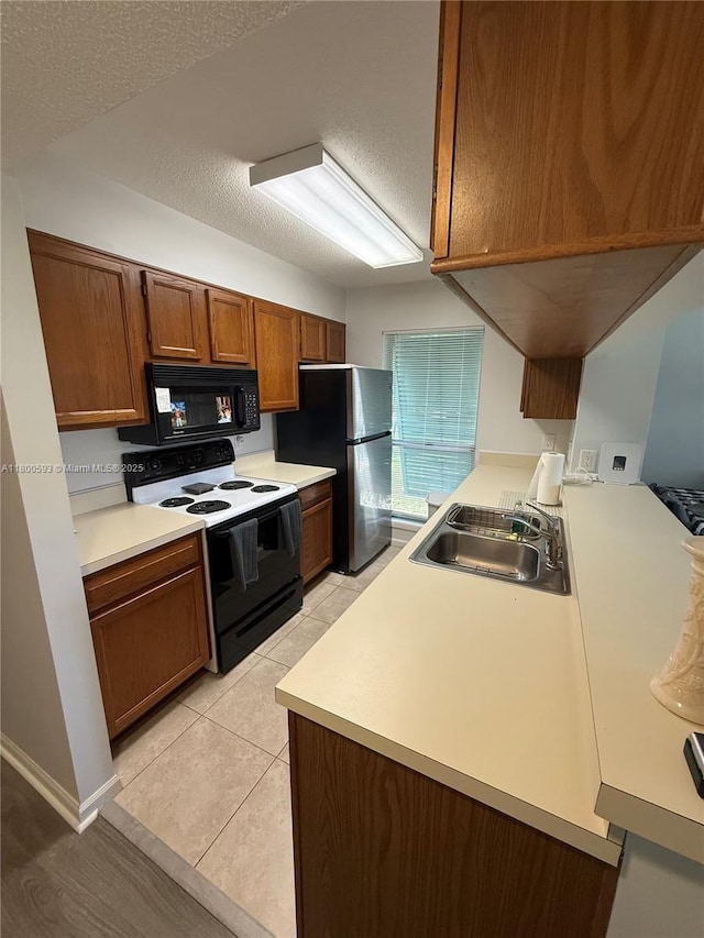 kitchen with range with electric stovetop, black microwave, freestanding refrigerator, a sink, and brown cabinetry