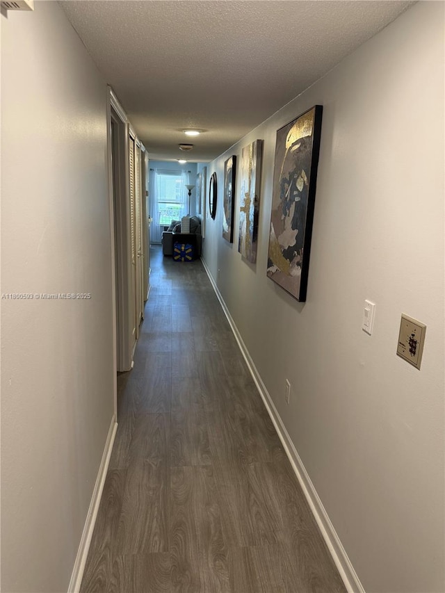 corridor with dark wood-style flooring, baseboards, and a textured ceiling
