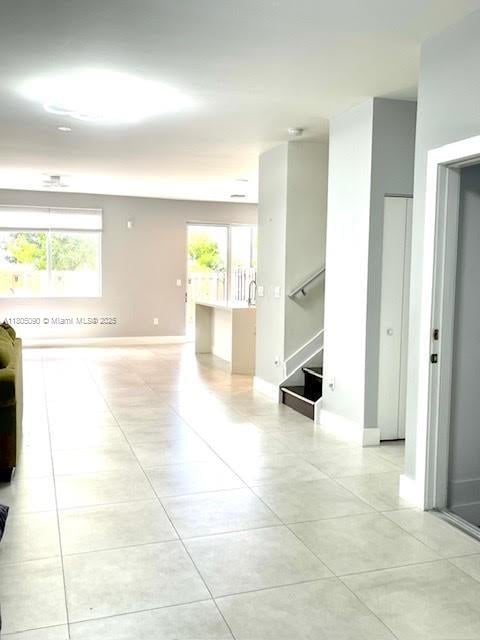 corridor with light tile patterned flooring, stairs, and baseboards