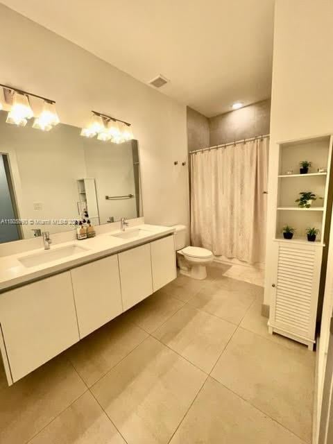 bathroom with tile patterned floors, toilet, double vanity, and curtained shower