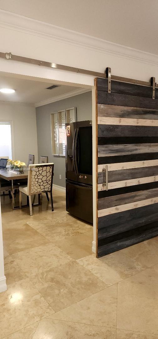 155 W 60th St, Hialeah, FL 33012 - detailed view of black fridge with ice dispenser, ornamental molding, a barn door, and baseboards