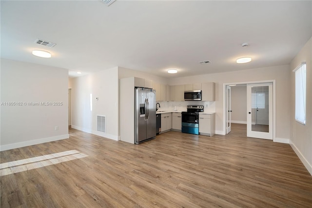 kitchen featuring stainless steel appliances, light countertops, a sink, light wood finished floors, and baseboards