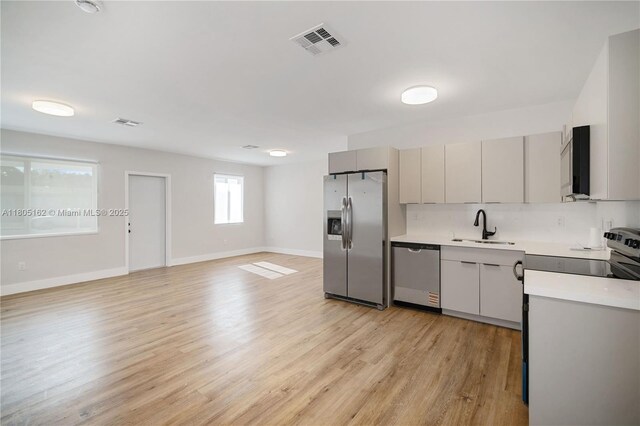kitchen with appliances with stainless steel finishes, a sink, light countertops, light wood finished floors, and baseboards