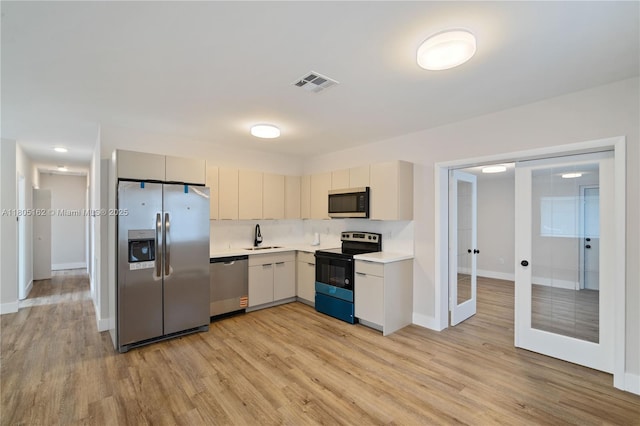 kitchen with appliances with stainless steel finishes, a sink, light countertops, french doors, and light wood-style flooring