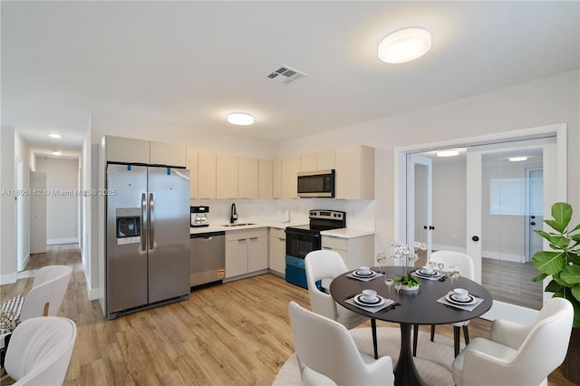 kitchen featuring appliances with stainless steel finishes, a sink, light countertops, light wood-type flooring, and french doors