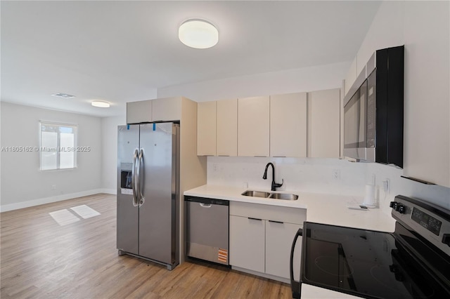 kitchen with appliances with stainless steel finishes, a sink, light countertops, light wood-style floors, and baseboards