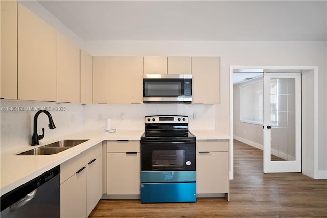 kitchen featuring stainless steel appliances, a sink, cream cabinetry, light wood-style floors, and light countertops