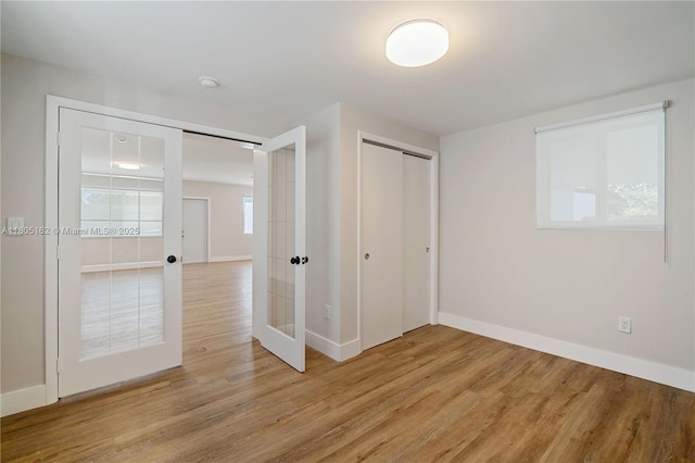 unfurnished bedroom featuring french doors, baseboards, light wood-type flooring, and a closet