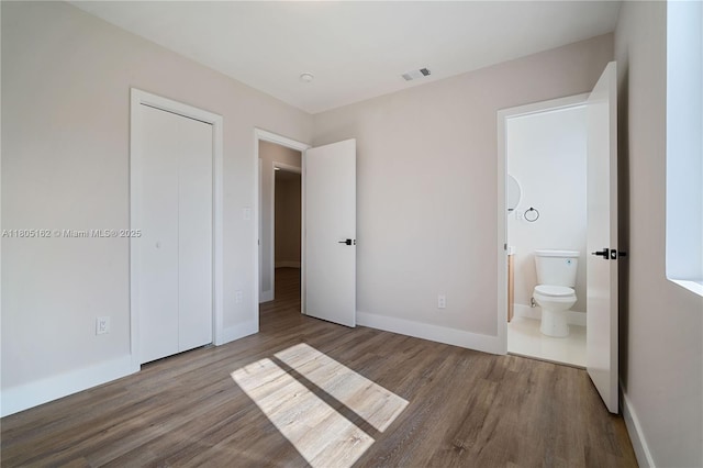 unfurnished bedroom with wood finished floors, baseboards, ensuite bath, and a closet