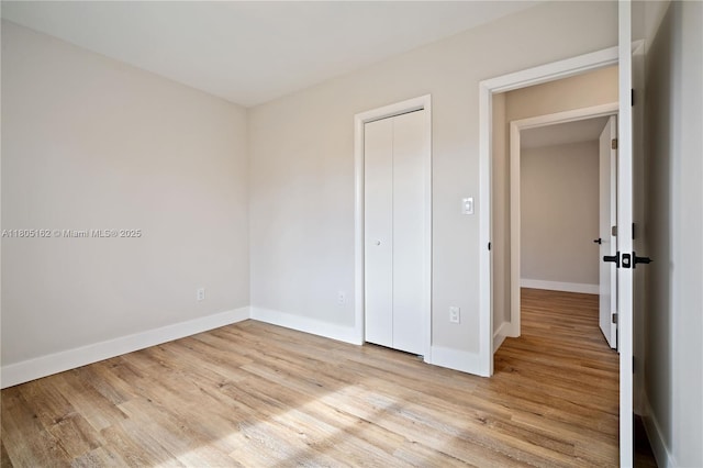 unfurnished bedroom featuring light wood-style floors, baseboards, and a closet