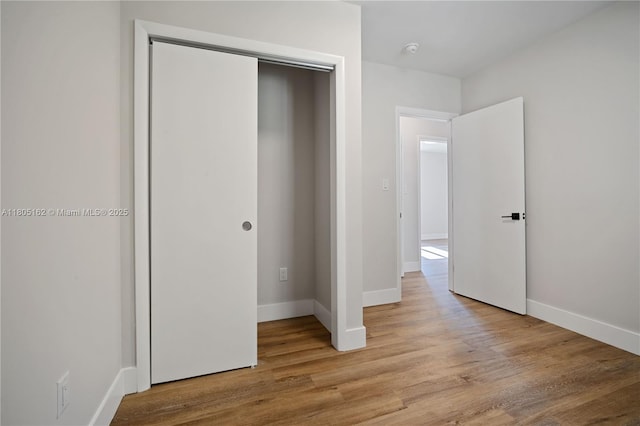 unfurnished bedroom featuring wood finished floors, baseboards, and a closet