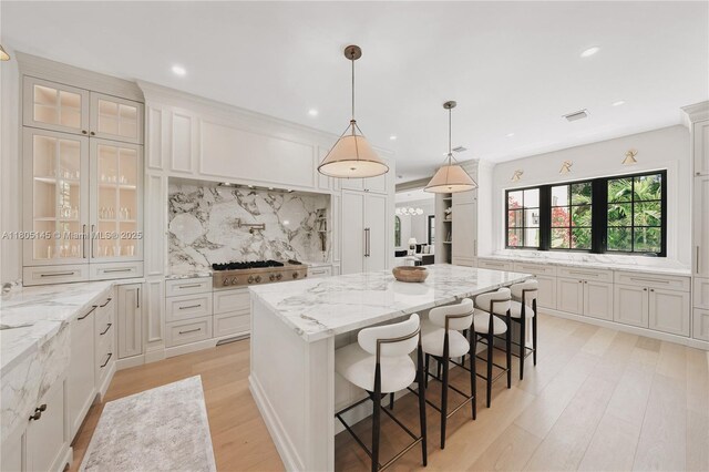 549 NE 59th St, Miami, FL 33137 - kitchen featuring stainless steel gas stovetop, a center island, decorative backsplash, light wood-style flooring, and glass insert cabinets