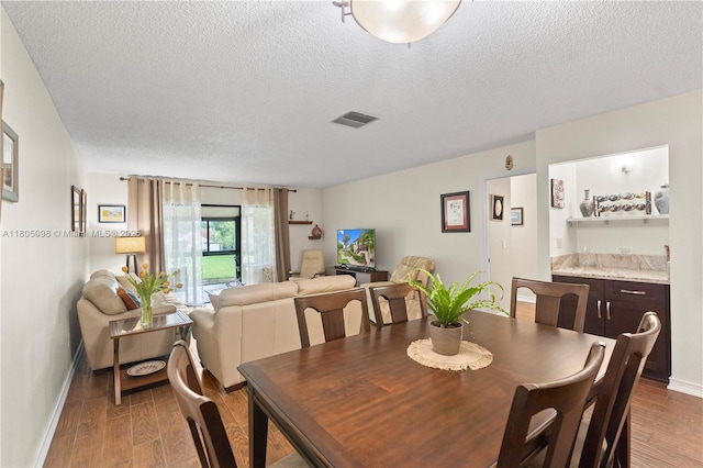 dining room with baseboards, a textured ceiling, and wood finished floors