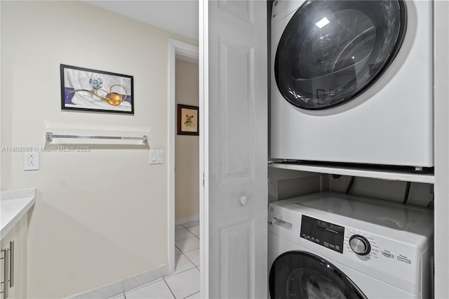 washroom with estacked washer and dryer, light tile patterned floors, and baseboards
