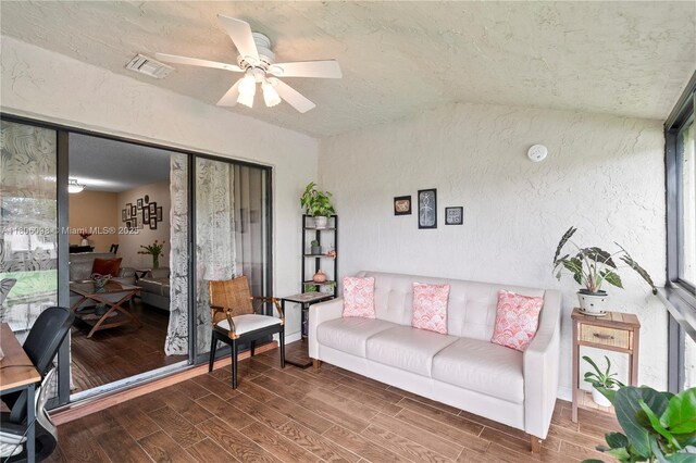 living area with a textured wall, a ceiling fan, wood finished floors, and lofted ceiling