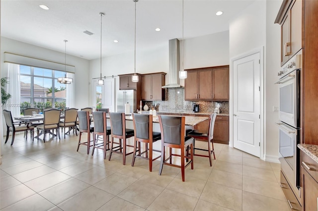 5474 S Sterling Ranch Cir, Davie, FL 33314 - kitchen featuring wall chimney range hood, appliances with stainless steel finishes, decorative backsplash, a kitchen breakfast bar, and a center island