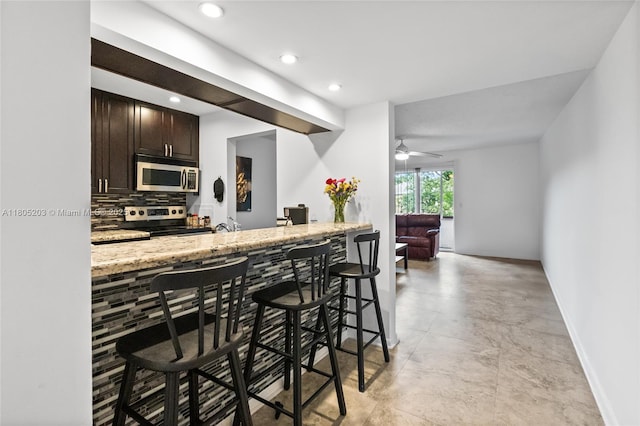 10772 La Placida Dr Unit 7-203, Coral Springs, FL 33065 - kitchen with appliances with stainless steel finishes, backsplash, dark brown cabinetry, a kitchen breakfast bar, and light stone counters