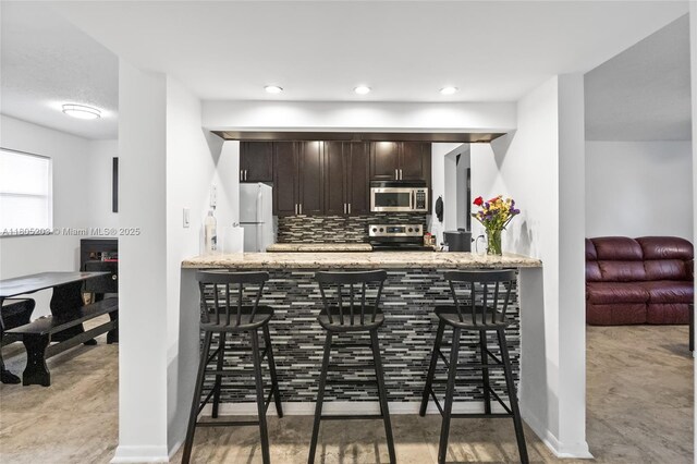 10772 La Placida Dr Unit 7-203, Coral Springs, FL 33065 - kitchen with appliances with stainless steel finishes, dark brown cabinetry, a peninsula, decorative backsplash, and light stone counters