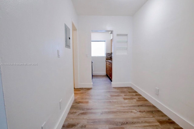 corridor with light wood-style flooring, electric panel, and baseboards