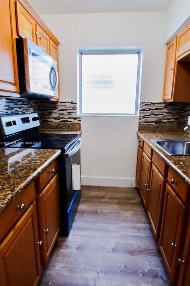 kitchen featuring appliances with stainless steel finishes, dark wood finished floors, a sink, backsplash, and baseboards