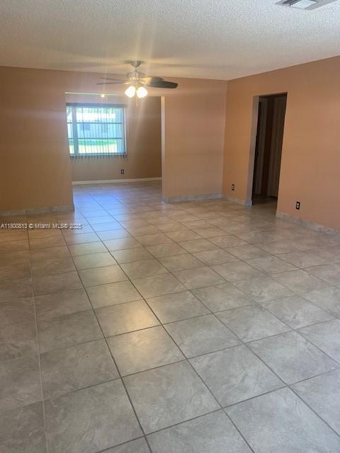 spare room with ceiling fan, a textured ceiling, light tile patterned flooring, and baseboards