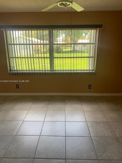 spare room with a ceiling fan, tile patterned floors, baseboards, and a textured ceiling