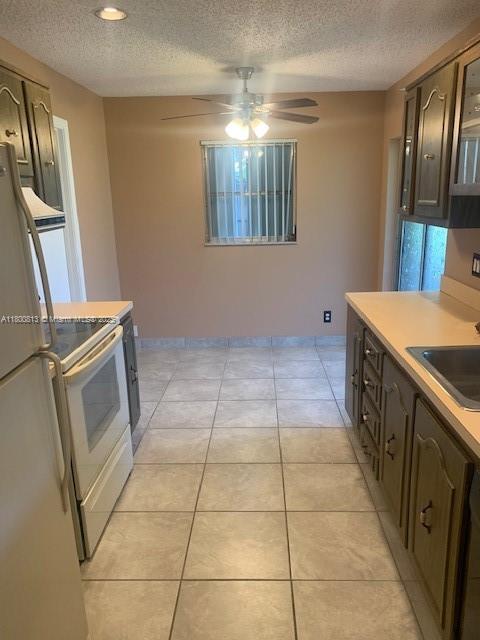 kitchen featuring white appliances, a textured ceiling, a sink, a ceiling fan, and light countertops